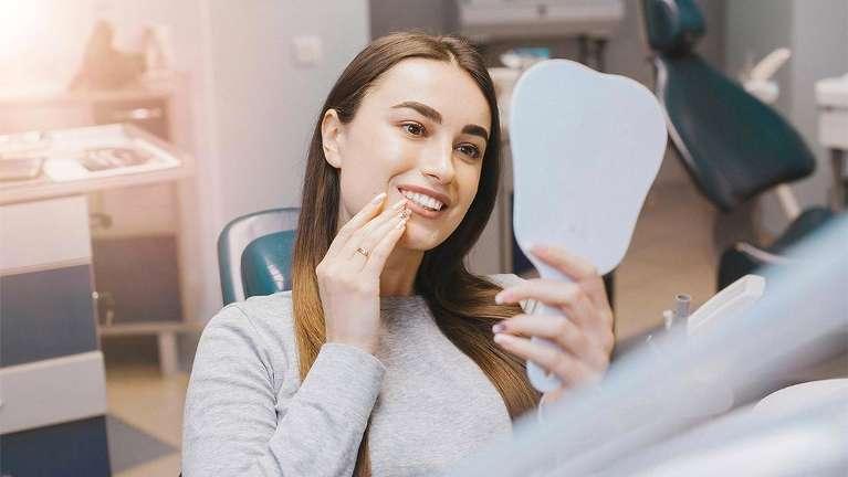 Woman looking into hand mirror after dental crown procedure in Mt Pleasant, SC