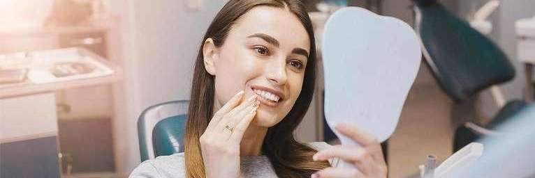 Woman looking at smile in hand mirror at cosmetic dentist in Mount Pleasant, SC