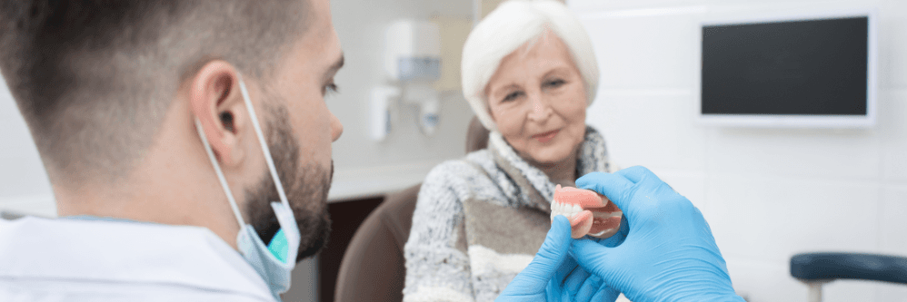 A dentist showing a set of dentures to an elderly patient.