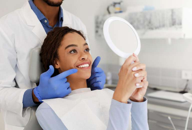 woman smiling into dental mirror after same-day crowns